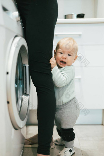 婴儿婴儿男孩孩子隐藏母亲腿要求注意多任务处理家庭家务厨房首页妈妈。孕妇离开