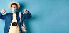 科维德夏天假期概念失望旅游梅迪克拉面具皱着眉头显示拇指负反馈旅行站蓝色的背景