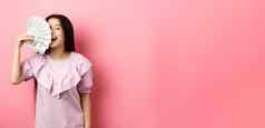 快乐丰富的亚洲女人显示钱微笑购物现金站衣服粉红色的背景