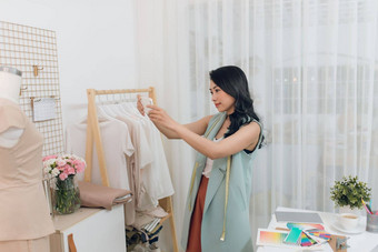美丽的年轻的亚洲时尚设计师采取照片工作智能<strong>手机女装</strong>裁缝工作室