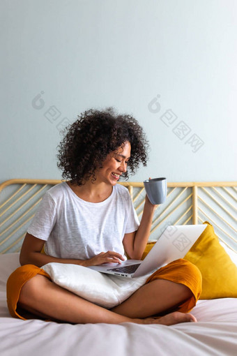 工作首页非洲美国年轻的女人坐着床上喝热咖啡打字移动PC垂直