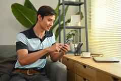 英俊的亚洲男人。自由职业者沟通社会网络移动电话坐着舒适的生活房间