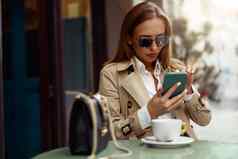 有吸引力的时尚的女人眼镜坐着咖啡馆阳台电话喝咖啡