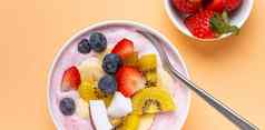 健康的早餐甜点酸奶碗新鲜的香蕉草莓蓝莓可可猕猴桃前视图最小的柔和的纸背景勺子