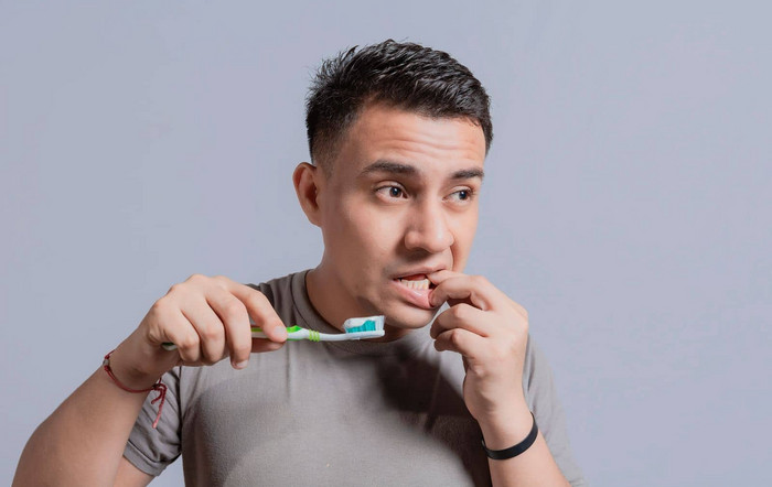 年轻的男人牙龈炎持有牙刷人持有牙刷口香糖