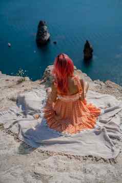 女孩红色的头发坐在回来查看器野餐毯子橙色衣服峰会山背景海岩石海