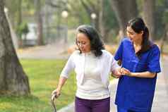 年轻的有爱心的女护士帮助高级女人走公园援助康复概念