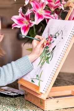 年轻的左撇子女孩绘画生活花紫色的百合水彩油漆画架