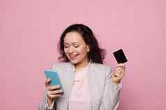 漂亮的女人持有智能手机信贷卡粉红色的背景人技术移动应用程序银行概念