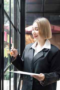 女孩亚洲女人企业家小公司把胶粘剂黏糊糊的笔记玻璃墙办公室分析制定业务策略