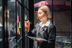女孩亚洲女人企业家小公司把胶粘剂黏糊糊的笔记玻璃墙办公室分析制定业务策略