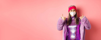 科维德流感大<strong>流行时尚</strong>概念快乐的亚洲高级女人聚会冠状病毒呼吸器显示竖起大拇指推荐穿脸面具粉红色的背景