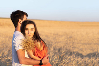 年轻的男人。拥抱女朋友日落小麦场复制空间爱在一起概念