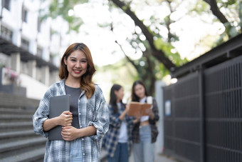 可爱的亚洲女孩学生持有书移动PC<strong>校园背景</strong>集团学生