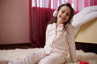 孩子女孩无线耳机坐着地毯穿着时尚的睡衣听舒缓的音乐