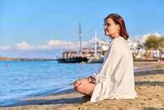 成熟的女人坐着莲花位置冥想海滩