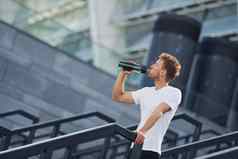 饮料水需要打破年轻的男人。运动型衣服锻炼在户外白天