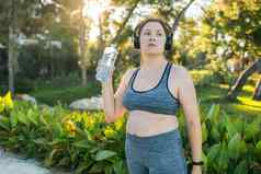 超重女人喝水慢跑公园肖像年轻的大号渴了女人瓶水在户外复制空间体育医疗保健重量失去健身幸福概念