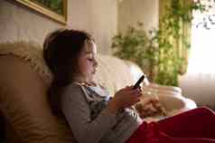 可爱的女孩看在线电影视频玩虚拟游戏移动电话坐着沙发上首页