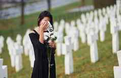年轻的女人黑色的衣服参观墓地白色十字架概念葬礼死亡