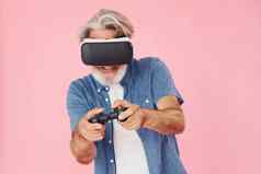 玩游戏虚拟现实眼镜操纵杆时尚的现代高级男人。灰色的头发胡子在室内