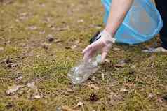 女人手手套收集把塑料瓶蓝色的垃圾袋志愿者清洗公园阳光明媚的明亮的一天清算污染生态塑料概念