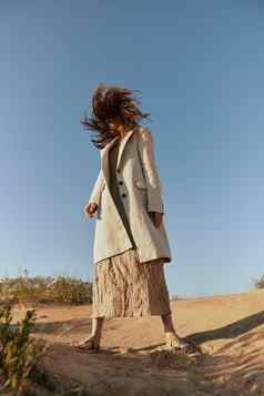 女人时尚夹克长裙子提出了站沙子背景清晰的天空