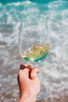 女人手白色酒玻璃绿松石地中海海泡沫波海滩背景