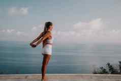 健身女人海快乐中间岁的女人白色运动服装练习早....在户外公园海滩视图女健身普拉提瑜伽例程概念健康的生活方式