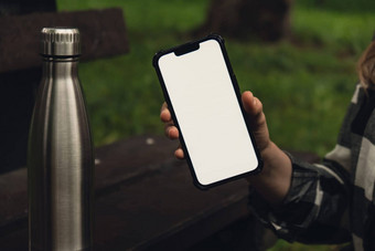 移动电话社会媒体白色屏幕模板移动应用程序可重用的钢热水瓶木板凳上可持续发展的生活方式塑料免费的浪费免费的生活绿色女人学生工作研究电话公园