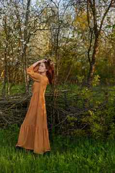 优雅的复杂的女人提出了站柳条栅栏别墅长橙色衣服矫直头发手