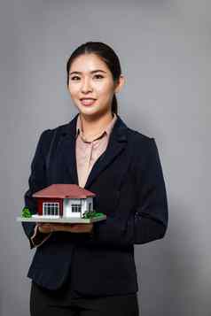 年轻的亚洲女人穿正式的西装持有房子模型热情的