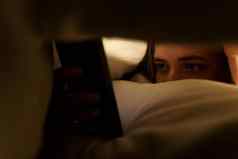年轻的女人谎言床上毯子浏览社会网络智能手机黑暗房间