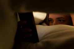 年轻的女人谎言床上毯子浏览社会网络智能手机黑暗房间