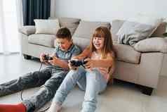 坐着地板上玩电子游戏孩子们有趣的国内房间白天