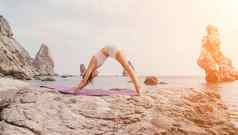 健身女人海快乐中间岁的女人白色运动服装练习早....在户外海滩火山岩石海女健身普拉提瑜伽例程概念健康的生活方式