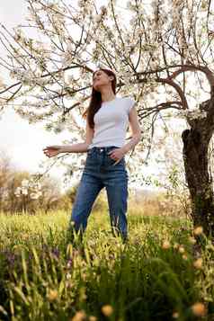 快乐的快乐女人牛仔裤光t恤摆姿势背景开花树