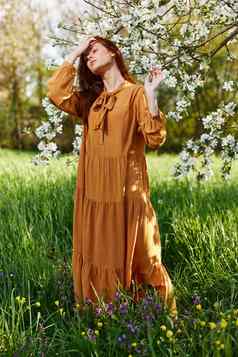 明亮的垂直照片有吸引力的女人长橙色衣服站开花树阳光明媚的温暖的天气矫直头发手关闭眼睛
