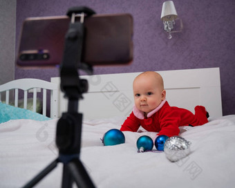 婴儿男孩穿着圣诞老人西装坐在床上生病的电话圣诞节视频调用