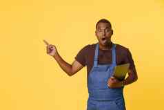 惊讶年轻的非洲美国烹饪蓝色的围裙搜索食谱在线平板电脑烹饪持有平板电脑手手势复制空间明亮的黄色的背景手