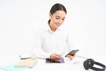 图像女商人坐在办公室数字平板电脑耳机智能手机检查客户消息调用员工白色背景