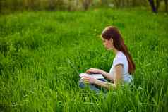 女自由职业者工作自然坐在草自然移动PC阳光明媚的夏天一天