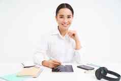 微笑亚洲女人坐在办公室作品数字平板电脑耳机智能手机工作文档平板电脑白色背景