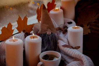 感恩节秋天万圣节概念庆祝秋天假期舒适的首页窗台上舒适审美大气秋天叶子Gnome香料蜡烛针织白色毛衣温暖的黄色的灯杯热茶喝