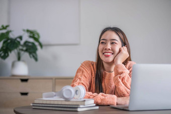 肖像微笑笑年轻的女人坐着表格穿无线耳机移动PC年轻的女看视频电影网络研讨会视频调用朋友家庭