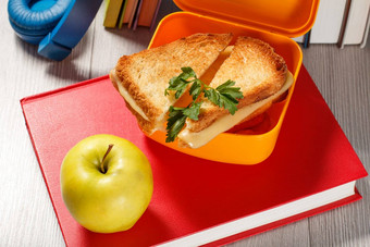 黄色的午餐盒子烤片面包奶酪绿色欧芹绿色苹果书背景