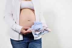 上腹部怀孕了女人期待婴儿持有新生儿衣服肚子白色背景怀孕周