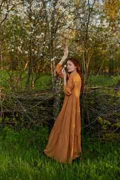 优雅的复杂的女人提出了站柳条栅栏别墅长橙色衣服提高手