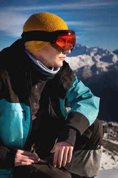 滑雪男人。坐着前山年轻的男人。蹲温暖的衣服阳光明媚的一天雪山
