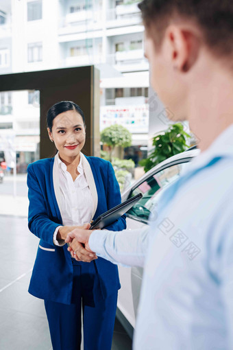 漂亮的微笑年轻的销售经理摇晃手客户问候显示汽车